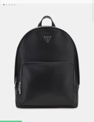 Svart ryggsäck från Guess - Stilren svart ryggsäck från Guess med klassisk rundad form och silverfärgad dragkedja. Väskan har ett stort huvudfack och en praktisk ytterficka framtill, samt Guess-logga i metall på framsidan. 