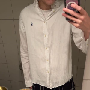 Vit linneskjorta från Polo Ralph Lauren - Vit linneskjorta från Polo Ralph Lauren i storlek XL/176 barnstorlek, tillverkad i linne. Klassisk button-down krage, långa ärmar och knappar framtill. Diskret blå Polo-logga broderad på bröstet. Jättebra skick på den, har endast använt denna 2-3 gånger så den är som en ny. Ordinarie pris på den är 1100kr. Hör av er om ni har frågor! OBS hör även har er om ni vill ha fler bilden på skjortan. 