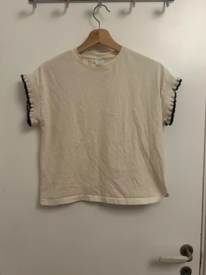 Beige topp med volangärmar från Zara - Säljer en beige topp från Zara med korta ärmar som har volangdetaljer och svart kant. Toppen har rund hals. Är i storlek xs men passar även mig som har xs.