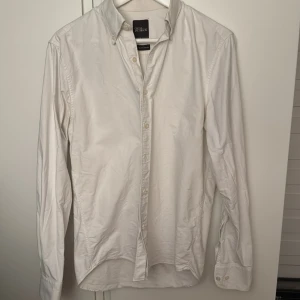 Vit oxfordskjorta Oscar Jacobson - Klassisk vit oxfordskjorta från Oscar Jacobson i regular fit. Skjortan har knappar framtill, button down-krage och är tillverkad i kraftig bomull. Perfekt för en clean och stilren look.