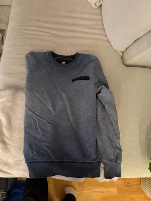 Blå sweatshirt från G-Star RAW - Snygg blå sweatshirt från G-Star RAW i storlek S. Tröjan har en mörkare blå ton, rund hals och en diskret bröstdetalj. Perfekt för dig som gillar stilrena och bekväma plagg. Materialet är mjukt och känns skönt mot huden. Passar dig som vill ha en enkel men cool look.