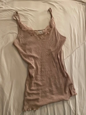 Beige ribbad linnetopp med spets - Säljer en rosa ribbad linnetopp från Saint Tropez  med smala axelband och snygg spetsdetalj runt halsringningen. Toppen är figurnära och har en mjuk, stretchig känsla som gör den superbekväm. Perfekt för dig som gillar en feminin och chill stil.