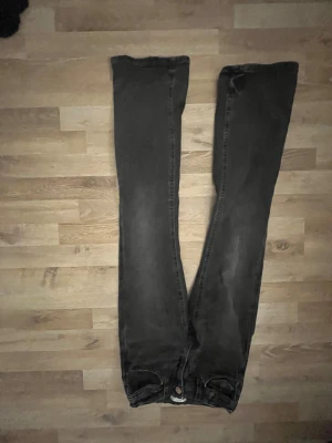 Svarta jeansbyxor från Gina Tricot - Svarta jeansbyxor från Gina Tricot med raka ben och snygga fickor bak, dekorerade med silvriga paljettdetaljer i form av rosetter. Byxorna har klassisk knappstängning och bälteshällor. Perfekta för dig som gillar en unik touch på dina jeans.