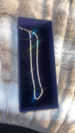 Swarovski diamant halsband - Säljer ett elegant halsband från Swarovski med gnistrande kristaller i rad på en silverfärgad kedja. Halsbandet har en klassisk och stilren design som verkligen drar blickarna till sig. Perfekt för dig som gillar att glänsa och vill ha något extra till din look.