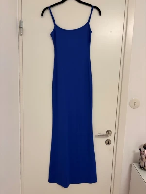 Blå långklänning från Bershka - Säljer en stilren blå långklänning från Bershka med smala axelband och figurnära passform. Klänningen har en enkel, minimalistisk design och är tillverkad i ett mjukt, stretchigt material som känns bekvämt mot huden. Perfekt för dig som gillar en clean och modern look.