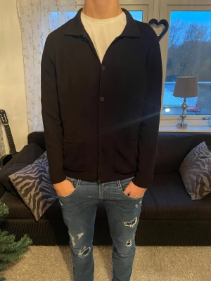 Svart kofta från Massimo Dutti - Svart kofta från Massimo Dutti i 100% bomull. Klassisk design med krage, knappar framtill och två praktiska fickor. Långärmad och med en clean look som funkar till jeans eller chinos. Perfekt för dig som gillar stilrena och enkla plagg.