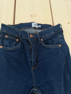 Mörkblå bootcut jeans med dragkedja - Snygga mörkblå jeans från 157 med klassisk femficksdesign, kopparfärgade nitar och dragkedja. Jeansen har bootcut-ben och kontrastsömmar som ger en schysst look. Perfekta för dig som gillar en retrostil och vill ha ett par jeans som sticker ut.