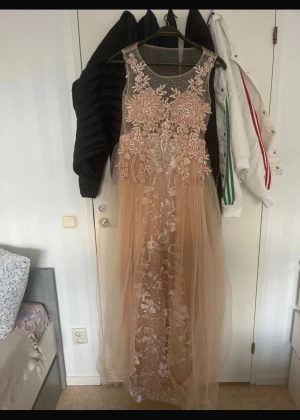 Balklänning med diamanter eller festklänning  - Magisk långklänning i champagnefärg med transparent mesh upptill, broderade blommor, pärlor och glittriga detaljer. Kjolen är i flera lager tyll med broderade blommor som ger en drömmig känsla. Perfekt för bal eller student. Ärmlös och med rund halsringning.