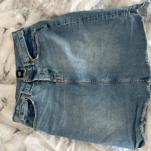 Ljusblå jeanskjol från 157 - Säljer en klassisk ljusblå jeanskjol från 157 med rå kant nertill och femficksmodell. Kjolen har knapp och dragkedja framtill samt bälteshällor. Perfekt för dig som gillar en enkel och tidlös denimstil.