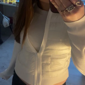 Vit jacka från Gina  med dragkedja - Säljer en fräsch vit pufferjacka med quiltade detaljer och dragkedja framtill. Jackan har långa ärmar, ribbade muddar och en croppad passform. Perfekt för dig som gillar en clean och stilren look.