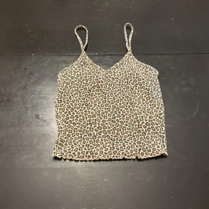 Leopardmönstrad linnetopp med smala band - Säljer en leopardmönstrad linnetopp med smala axelband och v-ringad hals. Toppen är i stretchigt material och har en beige bas med svarta och bruna leopardfläckar. Perfekt för dig som vill sticka ut lite extra.