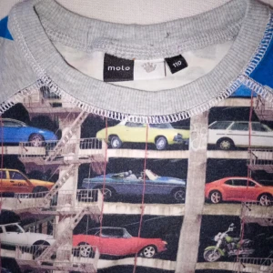 Molo långärmad tröja med bilar - Cool långärmad tröja från Molo med färgglatt biltryck på framsidan och grå ärmar med blå stjärnor. Tröjan har rund halsringning och är gjord i mjuk bomull, perfekt för dig som gillar unika prints och streetstyle.