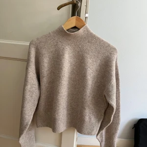 Beige stickad tröja & Other Stories - Supermjuk beige stickad tröja från & Other Stories med hög krage och ribbade detaljer vid hals, ärmslut och nederkant. Perfekt för lager-på-lager och chill höst- eller vinterstil. Enkel att matcha med jeans eller kjol.