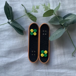 Fingerboard Mini Skateboard Set - Två fingerboards i färgglada designer med röda hjul och extra gröna/gula hjul. Båda brädorna har grip tape och är i gott skick, perfekta för tricks och samling. Inga synliga defekter eller större slitage.
