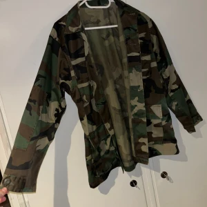 Camouflage parkajacka - Säljer en grön, brun och svart camouflage parkajacka. Jackan har flera stora fickor framtill, knappar och klassisk krage. Perfekt för dig som vill ha en streetig och avslappnad look. Finns en liten fläck vid högta bröstficka men inget som syns jätte tydligt eller stör användning. Bild kan fixas!