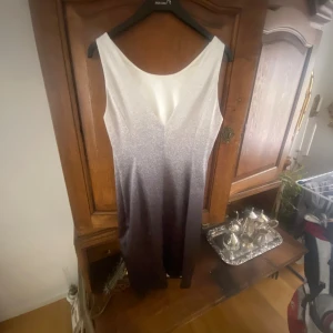 Glansig ombreklänning från Karen Millen - Supersnygg ärmlös klänning från Karen Millen med v-ringning och glansig ombre-effekt från vitt upptill till mörkgrått nertill. Figurnära passform och elegant siluett, perfekt för dig som vill sticka ut. Materialet känns lyxigt och skimrande. Passar 40/38.