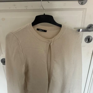 Beige kofta från Gina Tricot - Säljer en stilren beige kofta från Gina Tricot. Koftan är stickad, har rund halsringning och stängs med en knapp upptill. Perfekt att slänga över en topp för en chill och snygg look.