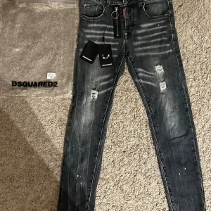 Svarta slim jeans från Dsquared2 - Snygga svarta slim jeans från Dsquared2 med slitningar och coola detaljer. Jeansen har dragkedja med ring, klassisk femficksdesign och vitgrå tvätt med slitna partier och färgstänk. Märkeslapp och etiketter kvar. Perfekt för dig som gillar streetstyle.