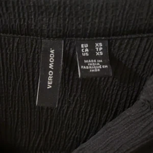 Svart långärmad klänning Vero Moda XS - Kamera don’t do it justice Svart klänning från Vero Moda i storlek XS. Klänningen har långärmade ärmar med knappar vid mudden och är gjord i ett tunt, lätt och strukturerat tyg som ger en snygg textur. Enkel och stilren design som passar perfekt till många olika looks.