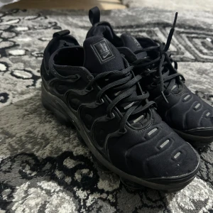 Nike Air Vapormax Plus - Svarta Nike Air Vapormax sneakers med cool, futuristisk design och synlig dämpning i sulan. Skorna har snörning, textilöverdel och detaljer i syntet. Perfekta för dig som gillar streetstyle och vill ha något som sticker ut.  ÄKTA