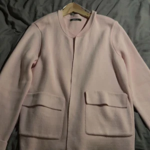 Ljusrosa cardigan med stora fickor - (Den är lite mer rosa i verkligheten)Snygg ljusrosa kappa i ull med minimalistisk design och stora fickor framtill🩷