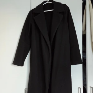 Svart lång kappa - Svart kappa med bälte i midjan. Passar bra som både höst och vinter jacka! Använd men inga defekter 