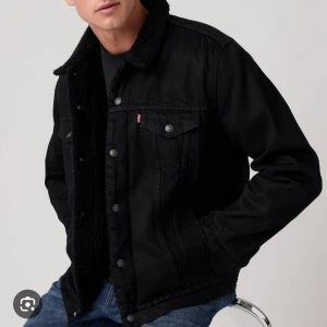 Svart teddyfodrad jeansjacka Levi's - Svart jeansjacka från Levi's med teddyfoder och krage i mjuk teddy. Klassisk modell med knappar framtill, två bröstfickor med lock och två sidofickor. Jackan har en rak passform och är perfekt för kyligare dagar.