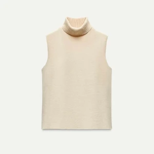Beige stickad väst med polokrage - Snygg beige stickad väst med hög polokrage. Perfekt att styla över en skjorta eller långärmad tröja för en trendig lager-på-lager-look. Västen har en rak passform och är ärmlös för en clean och minimalistisk vibe.