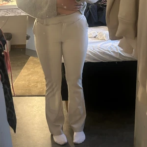 Beiga bootcut byxor med bälte - Snygga beiga byxor med bootcut och hög midja. Byxorna har ett medföljande bälte i samma färg och material, samt fickor både fram och bak. Perfekta för dig som gillar en stilren och trendig look.