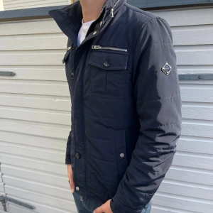 J.Lindeberg field jacket  - Snygg mörkblå field jacket från j Lindberg. Skick 8/10 riktigt bra har en knapp som gott halft sönder höger uppe fickan. Nypris ligger runt 3000kr men säljs nu för 1399kr. Hör gärna av er vid minsta lilla fundering!