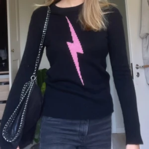100% kashmir zadig & Voltaire tröja  - Svart stickad tröja med en stor rosa blixt framtill. Tröjan har rund halsringning och långa ärmar. Perfekt för dig som vill ha en cool och edgy look med en färgklick.
