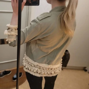 Grön jacka med virkade detaljer - Snygg ljusgrön jacka med virkade och broderade detaljer beige och vitt längs ärmslut och nederkant. Jackan har långa ärma och en loose passform. Perfekt för dig som vill sticka ut med coola detaljer och boho-vibe. SÅ perfekt till hösten!❤️