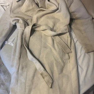 Beige kappa med bälte från H&M xl - Stilren beige kappa från H&M i storlek XL. Klassisk modell med bälte i midjan och diskreta fickor. Tidlös design med lång ärm och mjukt tyg som passar perfekt för kyligare dagar.