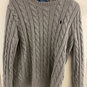 Grå kabelstickad tröja Polo Ralph Lauren - Kabelstickad grå tröja från Polo Ralph Lauren med klassisk rund halsringning och broderad logga på bröstet. Tröjan är långärmad och har ribbade muddar vid ärmslut och nederkant. Perfekt för lager-på-lager under kyliga dagar . Köpt från zalando för 2400kr mitt pris 550kr. Storlek S. pris går att diskuteras vid snabbaffär.