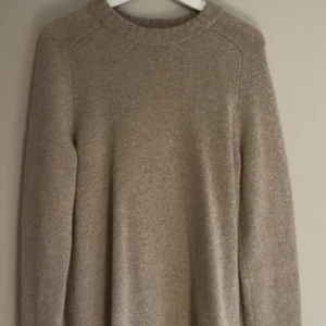 Beige stickad tröja från East West - Mysig beige stickad tröja från East West i lammull. Tröjan har rund halsringning, ribbade muddar och lång ärm. Perfekt för lager-på-lager under kyliga dagar. Tröjan är knappt använd då jag har växt ur den.  Nypris: 850:-