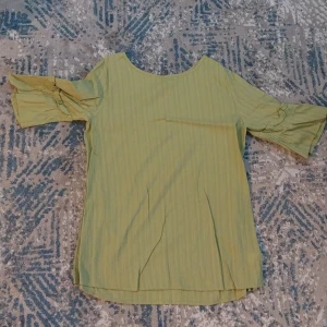 Grön blus med vida ärmar - Säljer en ljusgrön blus med subtila ränder och vida, korta ärmar med snygg rynkning vid axlarna. Blusen har en rund halsringning och är tillverkad i ett mjukt bomullsmaterial som känns skönt mot huden. Perfekt för dig som gillar en chill och trendig look.