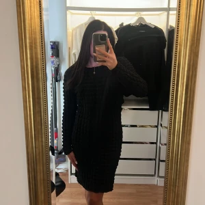 Svart långärmad strukturerad klänning - Säljer en svart långärmad klänning med coolt strukturerat tyg och kroppsnära passform. Klänningen är knälång och har rund halsringning. Perfekt för dig som gillar en stilren look med en twist.