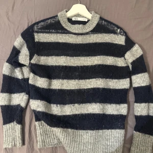 Randig stickad tröja från Zara - Mysig stickad tröja från Zara med breda marinblå och grå ränder. Tröjan har en loose passform, ribbade muddar och rund hals. Perfekt för lager-på-lager och chill dagar. Snygg till både jeans och kjol.