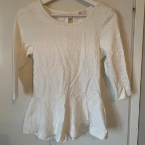 Vit peplumtop med strukturmönster - Säljer en vit peplumtop från C i storlek S. Toppen har ett snyggt strukturmönster framtill, rund halsringning och trekvartsärm. Modellen är figurnära upptill och har en volang nertill som ger en peplumeffekt. Perfekt att styla med jeans eller kjol.