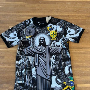 Nike Brasil grafisk fotbollströja | Kristusmotiv & CBF - .Säljer en Nike Brasil-fotbollströja med ett grafiskt svartvitt motiv av Kristusstatyn och brasilianska symboler. Tröjan har kortärmad modell, svart krage och broderat CBF-märke i gult. Tillverkad i Dri-FIT-material som andas – perfekt för träning, match eller streetwear.  ✔️ Lätt och ventilerande ✔️ Kortärmad, regular fit ✔️ Aldrig använd  Storlek: M Skick: Ny / aldrig använd  Passar dig som vill sticka ut på läktaren eller planen.
