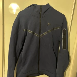 Blå Nike hoodie med dragkedja/ Nike tech - Säljer en marinblå hoodie från Nike i storlek M,  använd med vissa mindre märken.