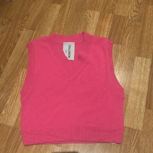 Rosa stickad väst från Collusion - En snygg rosa stickad väst från Collusion med v-ringning och ribbade kanter. Modellen är croppad och har en enkel, stilren look som passar perfekt till jeans eller kjol. Tillverkad i mjukt syntetmaterial för en bekväm känsla.