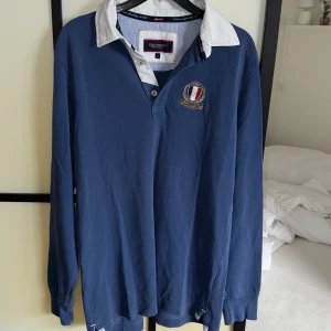 Blå långärmad pikétröja Galvanni - Säljer en blå långärmad pikétröja från Galvanni med vit krage och broderad logga på bröstet. Tröjan har klassisk pikéknäppning och är gjord i bomull, perfekt för en preppy look. Storlek L men skulle säga det passar mer M eller Stor S.