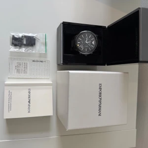 Svart klocka Emporio Armani AR-1451 - Stilren svart klocka från Emporio Armani, modell AR-1451. Har använts ett fåtalgånger, nypris 1490kr. Det finns inga repor eller skador på klockan. Länken är i blankt rostfritt stål och extra länkar medföljer. Levereras i originalbox. Hör gärna av dig vid funderingar.