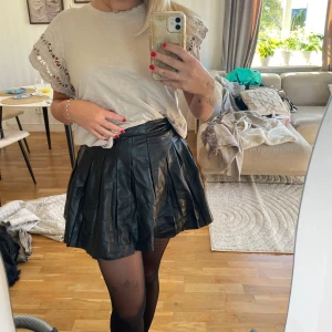 Plisserad svart skinnkjol - Säljer en svart plisserad kortkjol i skinnimitation. Kjolen har hög midja och breda, markerade veck som ger en snygg volym. Storlek M 