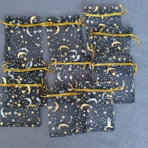 Godispåse/smmyckenpåse - Ny, 10st. Liten svart organzapåse med skimrande guld- och silvermönster av stjärnor och månar. Påsen har en smidig dragsko i guldigt snöre som gör den enkel att öppna och stänga. Perfekt för småsaker, smycken eller presenter.