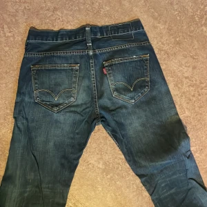 Levi's 504 Straight jeans blå - Säljer ett par Levi's 504 Straight jeans i mörkblå denim med klassiska kontrastsömmar och femficksdesign. Jeansen har rak passform och normal midja. Ikonisk Levi's-logga på bakfickan och slitna detaljer. Innerben 76cm längd 105cm