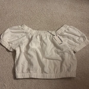 Vit croppad blus från Kappahl - Superfin vit croppad blus från Kappahl med puffiga korta ärmar och resår vid hals, ärmslut och nederkant. Tillverkad i ett lätt linnematerial som känns luftigt och fräscht. Perfekt för dig som gillar en söt och trendig look.