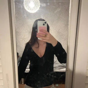 Svart ribbad stickad tröja NA-KD - Svart stickad tröja från NA-KD med djup v-ringning och ribbad struktur. Långärmad och i mjukt material som sitter snyggt på kroppen. Perfekt för lager-på-lager och funkar året runt.