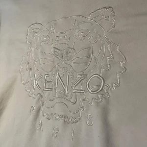 Vit sweatshirt från Kenzo med tigerbrodyr - Vit sweatshirt från Kenzo med ikonisk tigerbrodyr och texten 'Kenzo Paris' framtill. Tröjan har rund halsringning, långa ärmar och ribbade muddar. Perfekt för dig som vill ha en clean men ändå statement look. XL på lappen men sitter mer som en L, avslappnad  Längd 72 Bredd 53/54